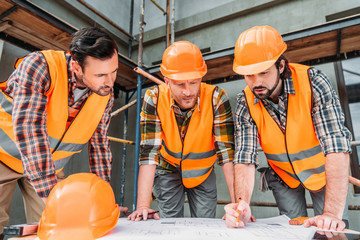 group of confident builders looking at building plan at construction site