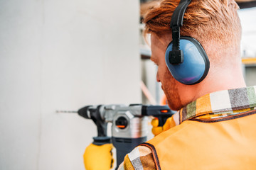 confident builder in noise reducing headphones using power drill at construction site