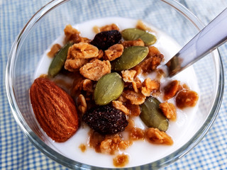 Healthy flavored yogurt in glass cup and spoon with cereal and granola isolated on the blue cloth background.