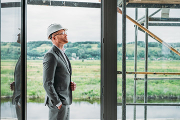 side view of handsome architect in suit and hard hat standing on terrace at construction site