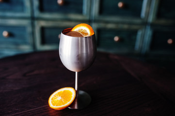 Alcoholic cocktail with ice and orange in silver glass on bar table.