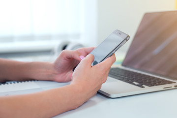 Close-up of female hands using modern smart phone while working at office with computer, businesswoman typing text message on her cellphone