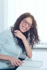 Smiling woman sitting at her desk in office. Happy business woman sitting in office with fingers touching her hair.