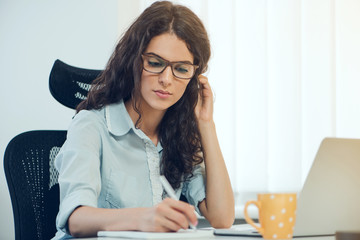 Cute young curly hair businesswoman sitting at the desk and writing on notebook