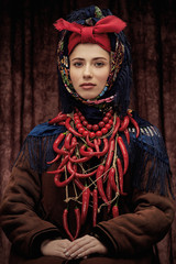 Portrait of young pretty woman sitting in ethnic winter costume with hands on her lap, wearing warm...