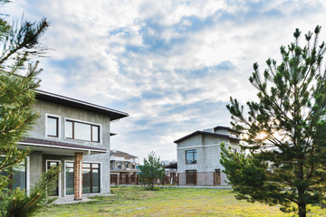 unfinished modern buildings with green yards on cloudy day with fir trees on foreground