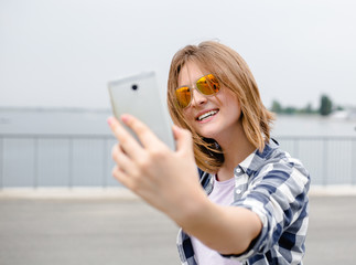 Young happy girl in hipster making selfie on phone