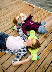 Two young girl in hipster outfit making selfie while lying with on wooden pier