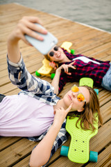 Two young girl in hipster outfit making selfie while lying with on wooden pier