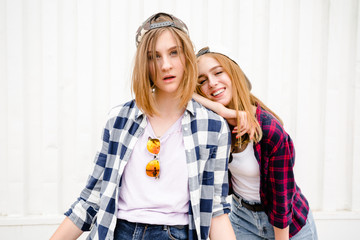 Two cheerful funny girl wearing checkered shirts posing against street wall at the street