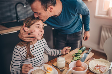 Father kissing daughter at breakfast table