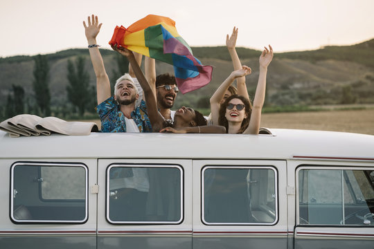 Smiling friends with rainbow flag standing in van