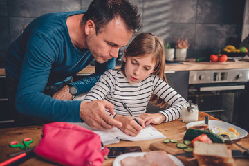 Father helping daughter with homework in kitchen