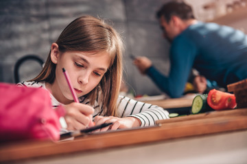 Girl using smart phone and doing homework at kitchen