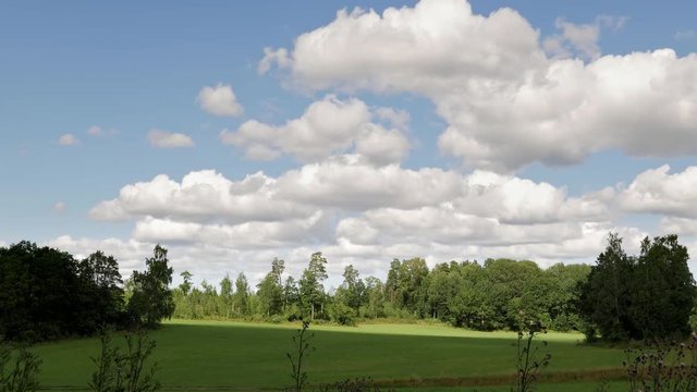 Clouds passing on blue sky. Over green field in Scandinavia.