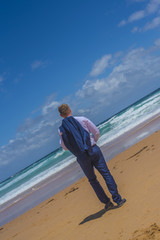 Man in blue suit standing at sandy beach watching the waves.