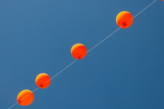 Orange balloons hanged on a wire with blue sky in the background. Beautiful wallpaper. No people.