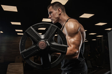 Fototapeta na wymiar A man is doing exercises in the gym, with dumbbells, against a dark background. Sportswear. The concept is strength, heavy training, crossfit, fitness, sports nutrition, diet, styrodes.