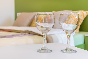 Two half full or half-empty wine glasses on night table next to the double bed in modern hotel bedroom. Valentines day or anniversary concept. Close up.
