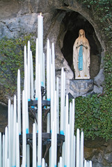 Candles at the Grotto of Lourdes, in France, with the image of Bernadette in the background