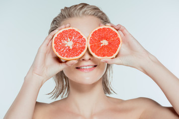 young woman holding grapefruit halves on eyes, isolated on grey
