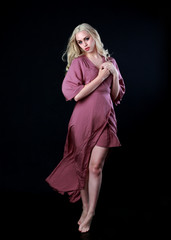 full length portrait of blonde girl wearing long purple dress. standing pose. black studio background.