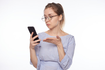 Young American blond businesswoman having specific appearance holding smart phone being confused while reading message from her business partner not understanding something. Occupation and career.