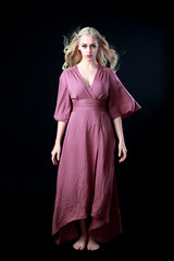 full length portrait of blonde girl wearing long purple dress. standing pose. black studio...