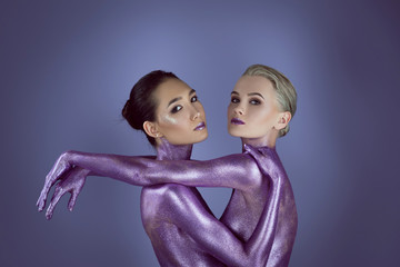 multicultural attractive girls in ultra violet glitter embracing each other, isolated on purple