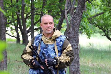 Obraz premium On the hunt. A military man hunter is standing with a firearm in the forest.