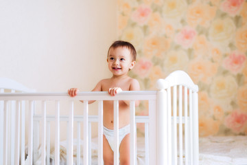 Little boy in white diaper standing in his bed. Portrait of happy smiling toddler in his bedroom