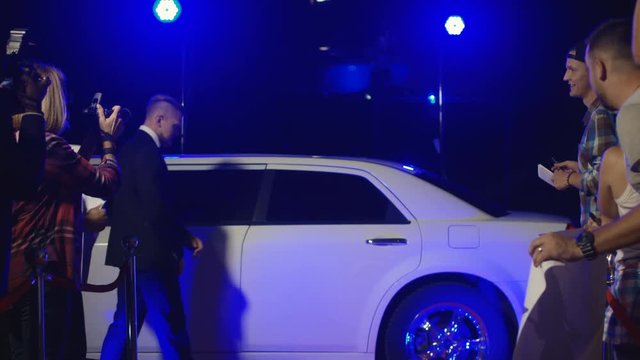 Group of rock musicians walking out of limo and giving autographs to fans while photographers taking shots on red carpet