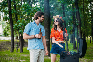 smiling couple in sunglasses with beer setting fire on grill together