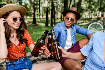 partial view of interracial friends clinking bottles of beer during picnic in park