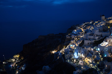 Whitewashed Houses and Windmill on Cliffs with Sea View at Night in Oia, Santorini, Cyclades, Greece