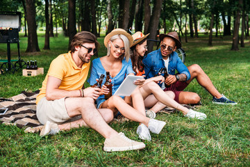 Fototapeta premium interracial friends with beer and table resting in summer park