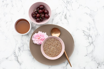 The concept of a healthy gluten-free Breakfast, linen porridge in a pink plate, herbal tea and cherries on a marble table.