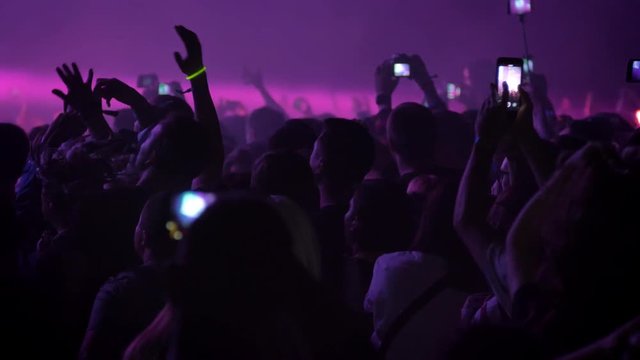 Footage of crowd cheering and recording video at rock concert at night