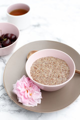 The concept of a healthy gluten-free Breakfast, linen porridge in a pink plate, herbal tea and cherries on a marble table.