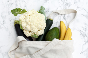 Set of products in a cotton bag on a marble table, bananas, avocado, eggplant, zucchini, cauliflower. The concept of zero waste.