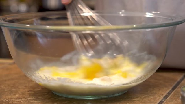 Closeup of whisking eggs, oil, and water in a glass mixing bowl
