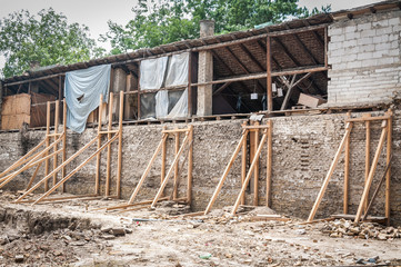 Wooden reinforcement beams holding old brick wall of the destroyed and damaged house collapsed in the earthquake or other natural disaster, selective focus