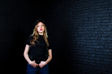 FBI female agent in cap and with gun at studio against dark brick wall.