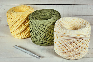 three coils of colored knitted yarn and a crochet hook on a white wooden background