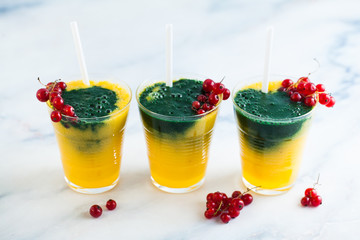 two colored fresh smoothies in glasses with fresh berries. orange banana juice with spirulina powder. detox breakfast. healthy eating