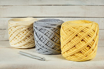 three coils of colored knitted yarn and a crochet hook on a white wooden background