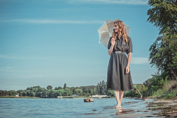 a woman walks along the river's edge hiding from the sun under lace umbrella and looking away