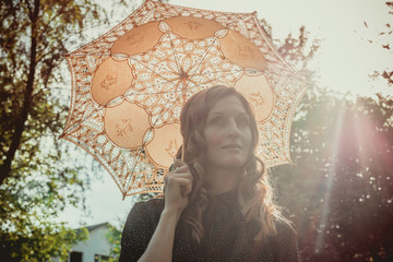 young woman hiding from the sun under white lace umbrella in backlight