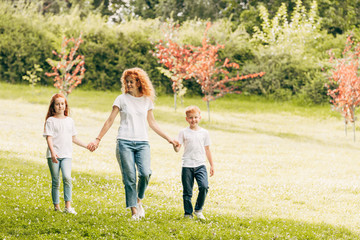 Naklejka na ściany i meble happy mother with two children holding hands and walking at park