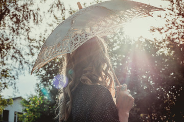 young woman hiding from the sun under white lace umbrella in backlight. Back view